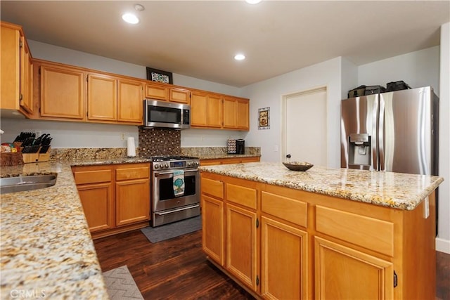 kitchen featuring sink, light stone counters, appliances with stainless steel finishes, dark hardwood / wood-style floors, and a kitchen island