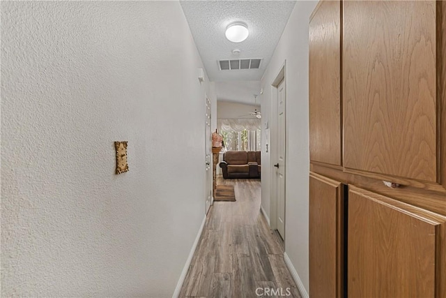 corridor with light hardwood / wood-style floors and a textured ceiling