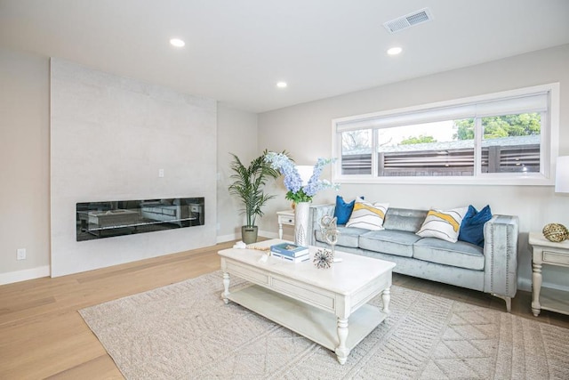 living room with a tiled fireplace and light wood-type flooring