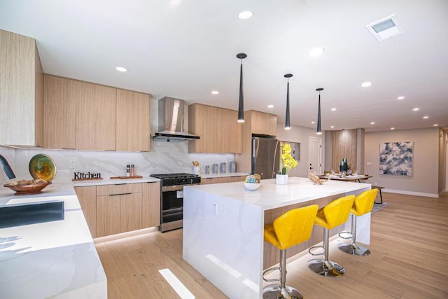 kitchen with appliances with stainless steel finishes, a center island, wall chimney range hood, and light brown cabinetry