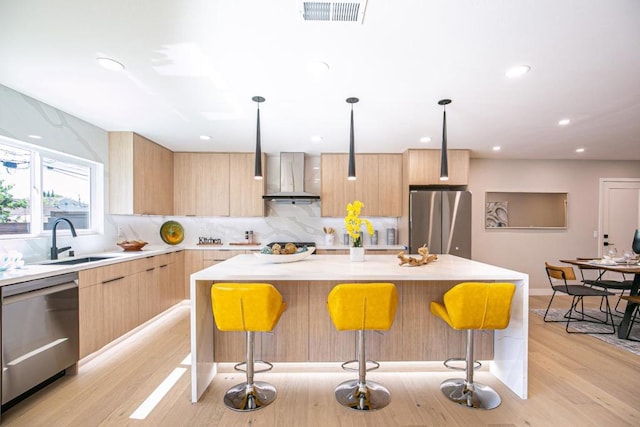 kitchen with a kitchen island, appliances with stainless steel finishes, a breakfast bar, and wall chimney range hood