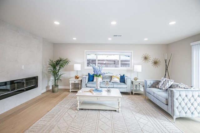 living room featuring a tiled fireplace and light wood-type flooring