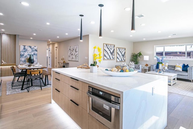 kitchen with light stone counters, decorative light fixtures, light hardwood / wood-style flooring, a large island, and oven