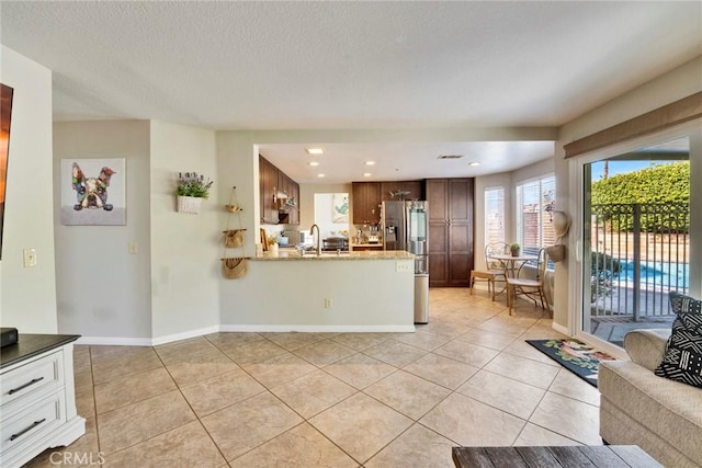 kitchen with light tile patterned floors, stainless steel fridge, light stone countertops, and sink