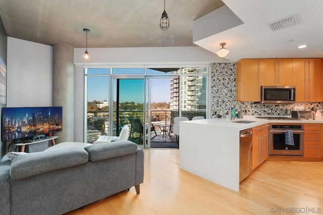 kitchen featuring appliances with stainless steel finishes, sink, decorative backsplash, hanging light fixtures, and light wood-type flooring