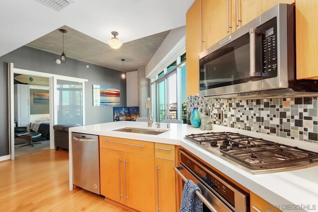 kitchen featuring pendant lighting, sink, backsplash, stainless steel appliances, and light hardwood / wood-style floors