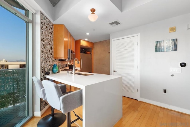 kitchen featuring a breakfast bar, appliances with stainless steel finishes, kitchen peninsula, light hardwood / wood-style floors, and decorative backsplash