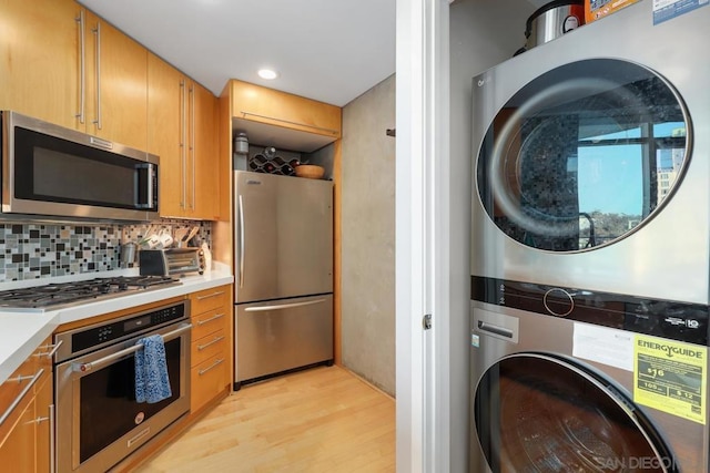 kitchen featuring stainless steel appliances, stacked washer and dryer, backsplash, and light hardwood / wood-style flooring