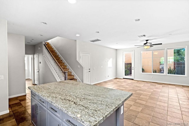 kitchen featuring ceiling fan, a center island, gray cabinetry, and light stone counters