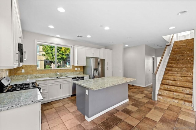 kitchen with sink, white cabinets, a center island, stainless steel appliances, and light stone countertops