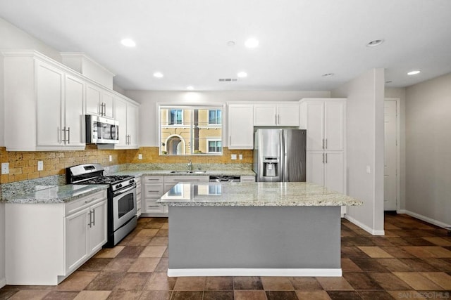 kitchen with white cabinetry, appliances with stainless steel finishes, light stone counters, and a kitchen island