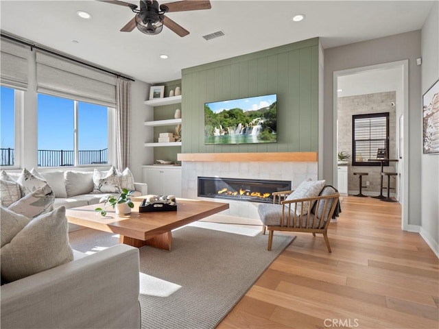 living room featuring a tiled fireplace, ceiling fan, and light wood-type flooring