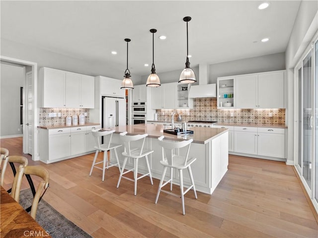 kitchen featuring pendant lighting, high end fridge, an island with sink, and white cabinets