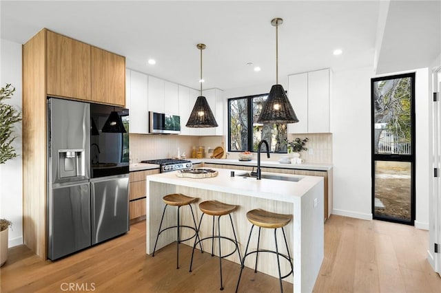 kitchen with sink, tasteful backsplash, a center island with sink, stainless steel appliances, and white cabinets