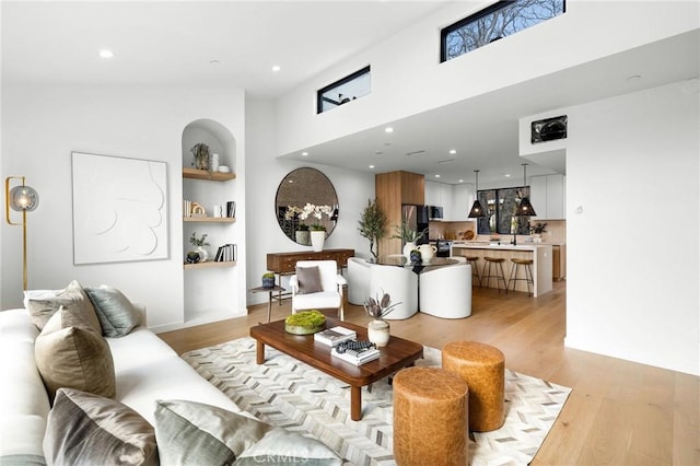 living room with a towering ceiling, built in features, and light hardwood / wood-style flooring