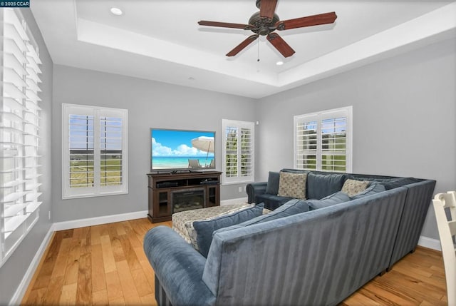 living room with wood-type flooring, a raised ceiling, and ceiling fan