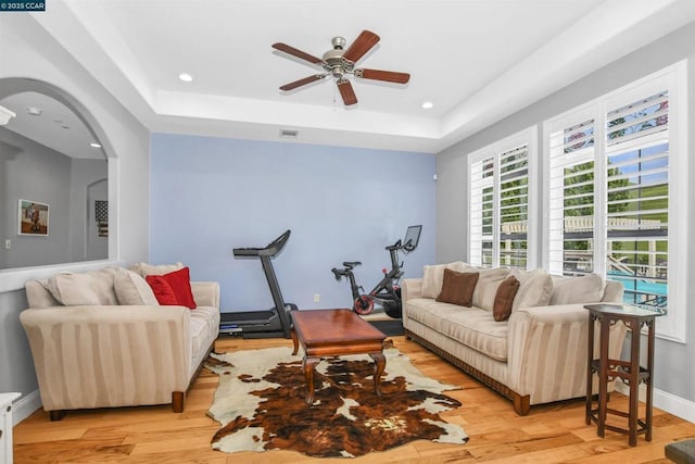 living room featuring ceiling fan, a tray ceiling, and light wood-type flooring