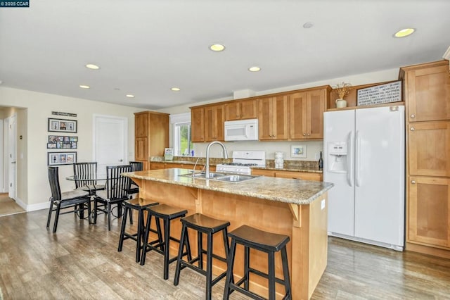 kitchen with sink, a breakfast bar area, hardwood / wood-style flooring, white appliances, and a kitchen island with sink