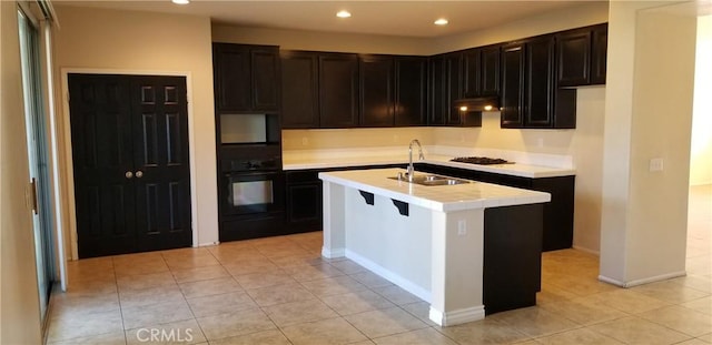 kitchen featuring sink, light tile patterned floors, gas cooktop, an island with sink, and oven