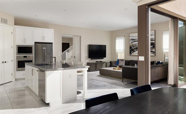 kitchen with white cabinetry, an island with sink, sink, a kitchen breakfast bar, and stainless steel appliances