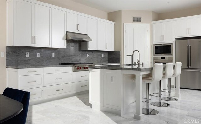 kitchen with appliances with stainless steel finishes, a kitchen island with sink, white cabinets, and a kitchen breakfast bar