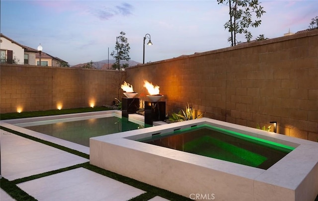 pool at dusk with an in ground hot tub