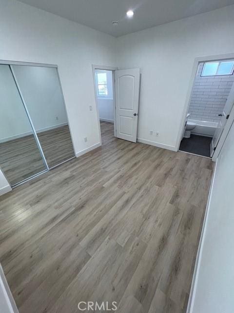 unfurnished bedroom with a closet, connected bathroom, and light hardwood / wood-style flooring