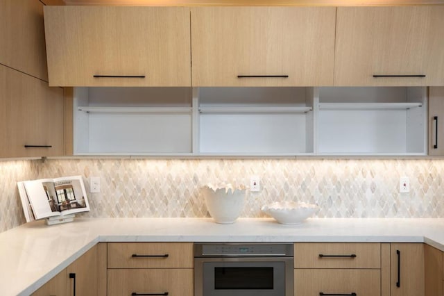 kitchen with stainless steel oven, backsplash, and light brown cabinets