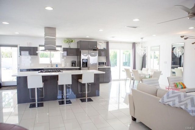 kitchen with a breakfast bar area, appliances with stainless steel finishes, a center island, tasteful backsplash, and island exhaust hood