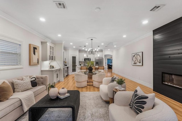 living room featuring crown molding, a chandelier, and light wood-type flooring