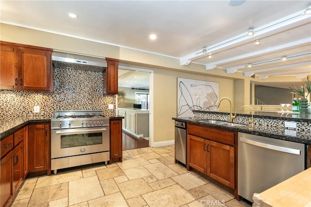 kitchen with sink, appliances with stainless steel finishes, dark stone counters, decorative backsplash, and wall chimney range hood