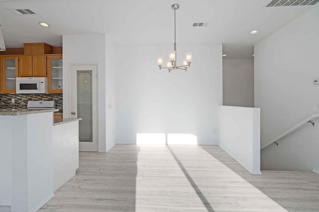 kitchen with tasteful backsplash, decorative light fixtures, a chandelier, light stone countertops, and light hardwood / wood-style floors