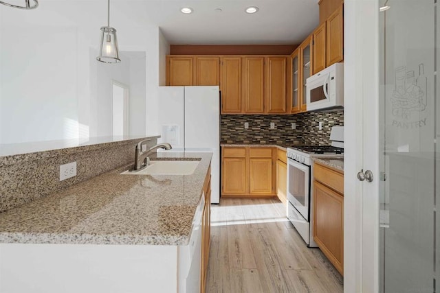 kitchen with sink, hanging light fixtures, light stone counters, light hardwood / wood-style floors, and white appliances