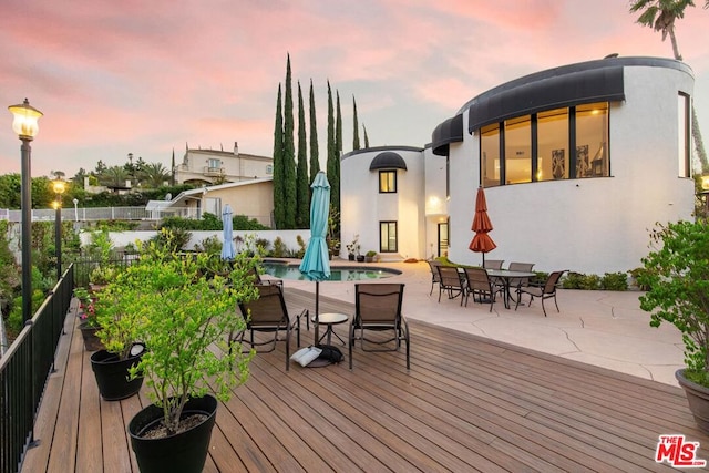 deck at dusk with a fenced in pool