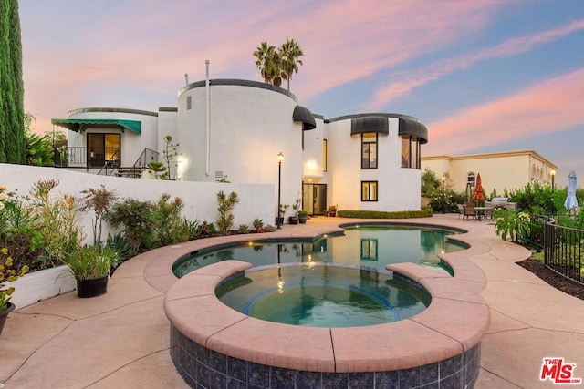 back house at dusk featuring a swimming pool with hot tub and a patio area