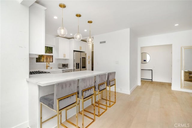 kitchen with a kitchen breakfast bar, kitchen peninsula, white cabinets, and appliances with stainless steel finishes