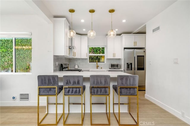 kitchen featuring sink, stainless steel fridge, range, white cabinets, and a kitchen bar