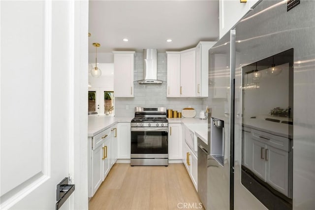 kitchen featuring appliances with stainless steel finishes, white cabinetry, backsplash, decorative light fixtures, and wall chimney exhaust hood