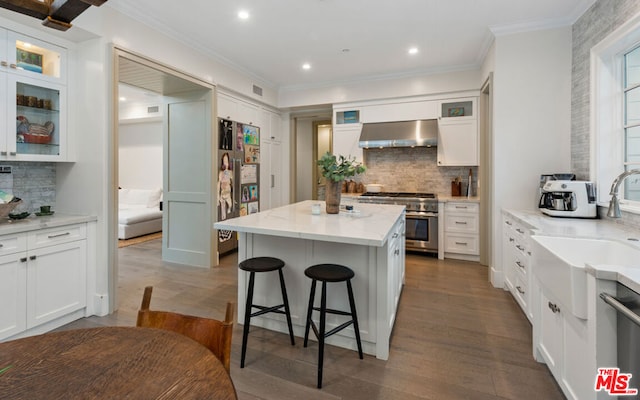 kitchen with wall chimney exhaust hood, sink, white cabinetry, a kitchen island, and stainless steel appliances