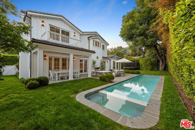 back of property with a balcony, french doors, a yard, a fenced in pool, and a patio area