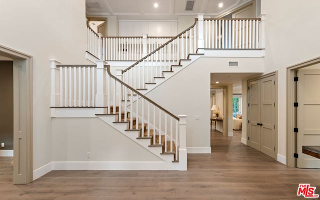 staircase with coffered ceiling, hardwood / wood-style floors, and a high ceiling