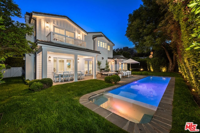 rear view of property featuring a patio, a balcony, a yard, and french doors