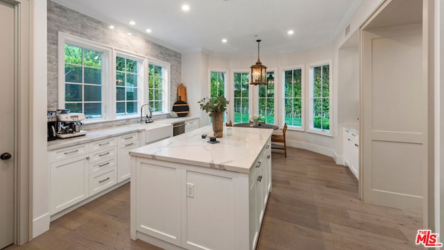 kitchen featuring pendant lighting, white cabinetry, ornamental molding, a center island, and light stone counters