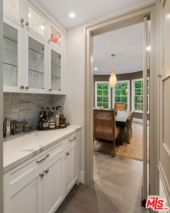 bar featuring light stone counters, decorative backsplash, pendant lighting, and white cabinets