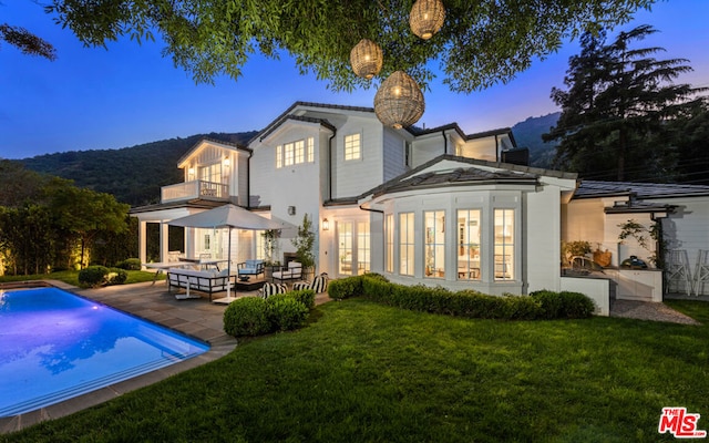 back house at dusk featuring a patio, a balcony, outdoor lounge area, a yard, and french doors