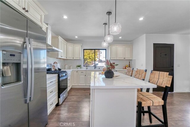 kitchen featuring a kitchen breakfast bar, a kitchen island, pendant lighting, stainless steel appliances, and light stone countertops