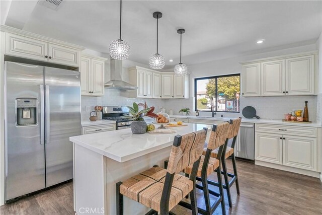 kitchen featuring pendant lighting, appliances with stainless steel finishes, a center island, dark hardwood / wood-style flooring, and wall chimney exhaust hood