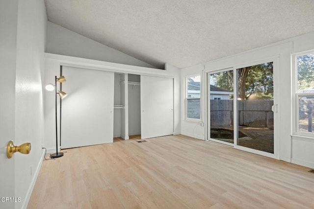 unfurnished bedroom featuring vaulted ceiling, a textured ceiling, access to exterior, and light wood-type flooring