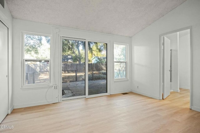 doorway to outside with lofted ceiling, a textured ceiling, and light wood-type flooring