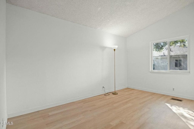 empty room featuring lofted ceiling, light hardwood / wood-style flooring, and a textured ceiling